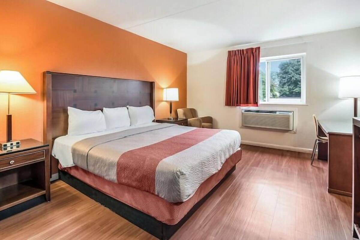 Habitación de hotel con una cama grande, dos mesitas de noche con lámparas, un escritorio y una ventana con cortinas.