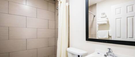 A bathroom with a shower, toilet, sink, and a mirror.