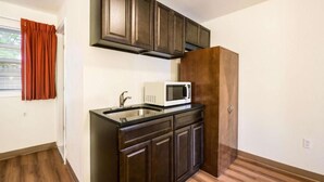 A compact kitchen with dark cabinetry, a white microwave, and a wooden cabinet.