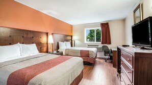 Habitación de hotel con dos camas, un escritorio, un televisor y una ventana con cortinas.