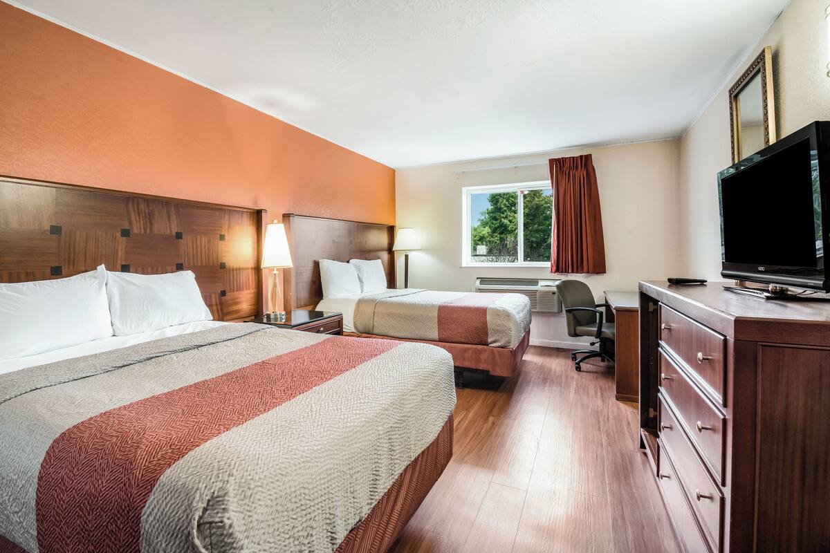 Habitación de hotel con dos camas, un escritorio, un televisor y una ventana con cortinas.