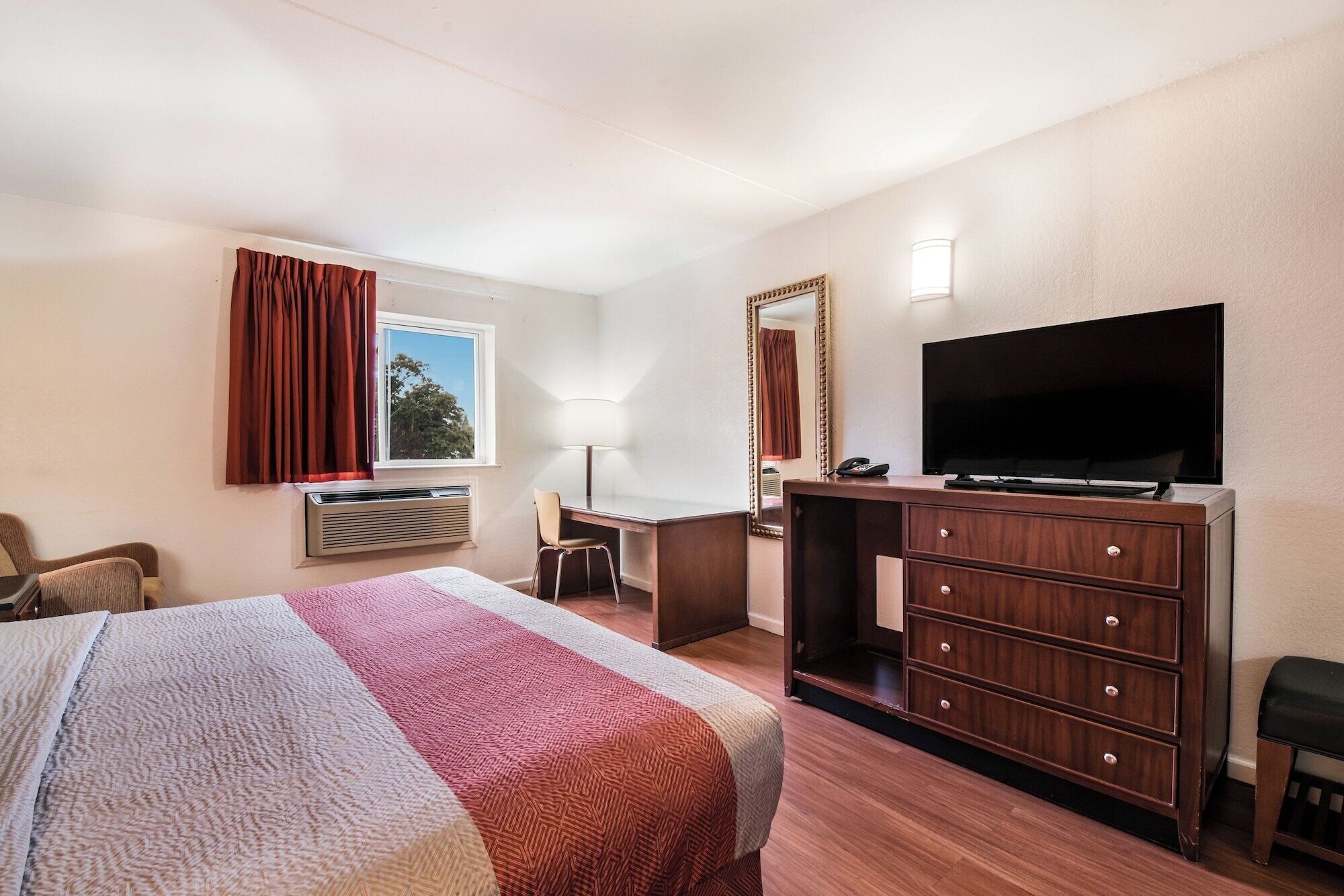 Una habitación de hotel con cama, escritorio, televisor y cómoda.