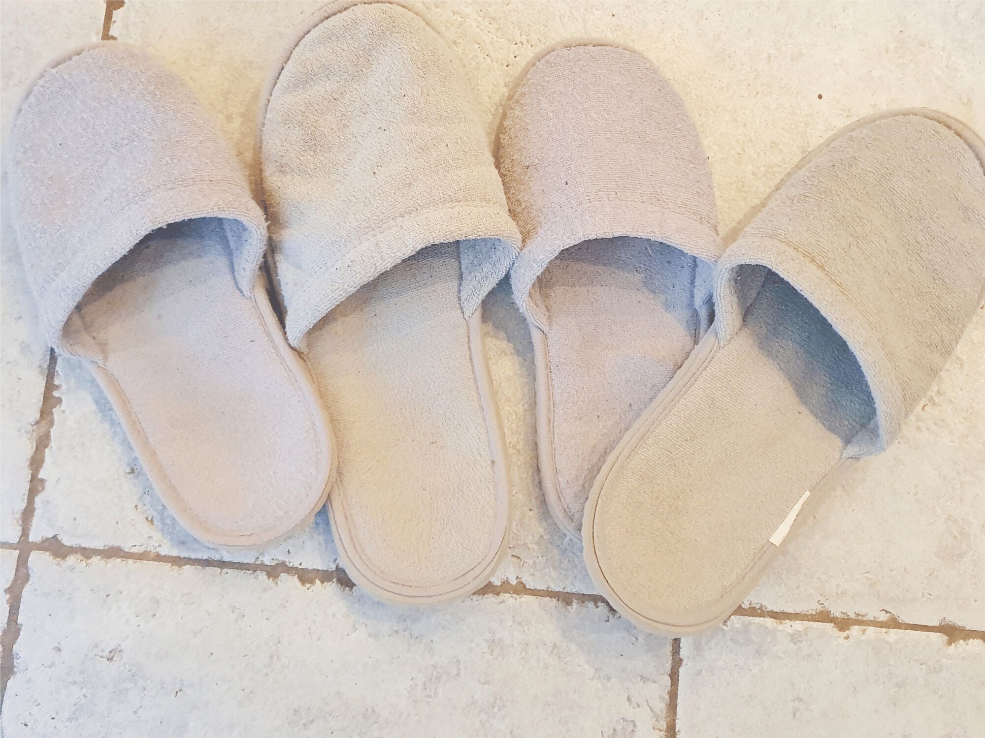 Un par de pantuflas color beige con superficie texturizada, sobre un piso de baldosas.