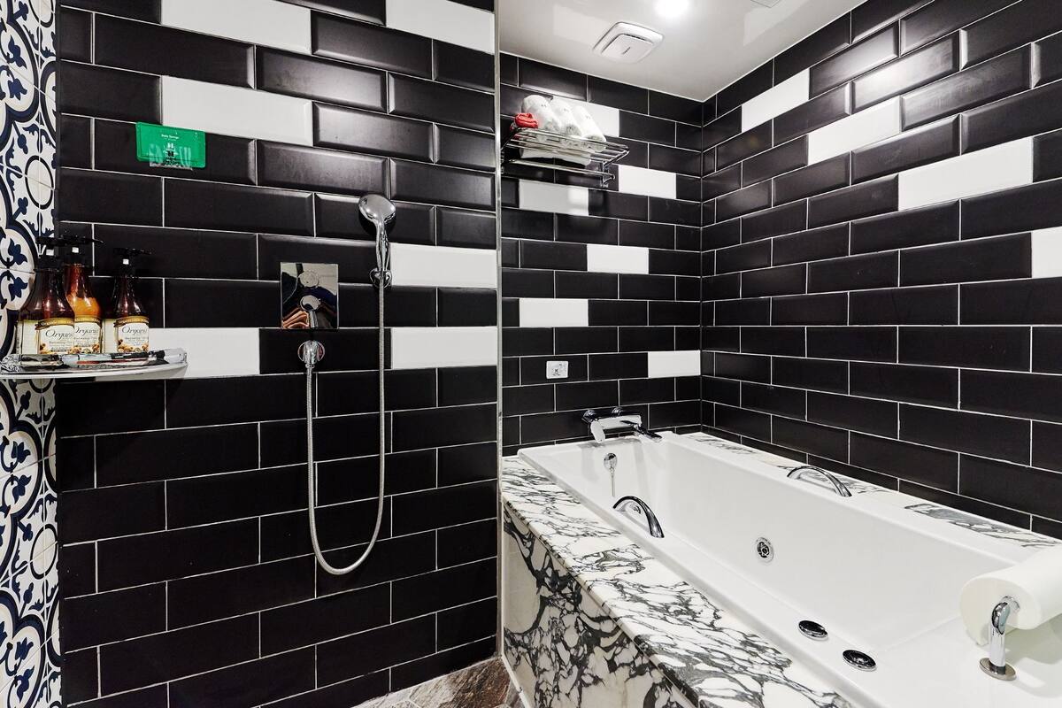 A bathroom with black and white tiled walls, a white bathtub with a marble-like pattern, and a shower area with a handheld showerhead.