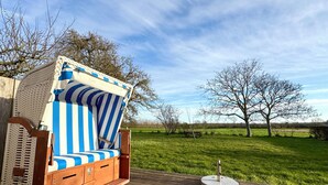 En træterrasse med et udendørs siddeområde med striber, et picnicbord og en græsplæne med træer i baggrunden.