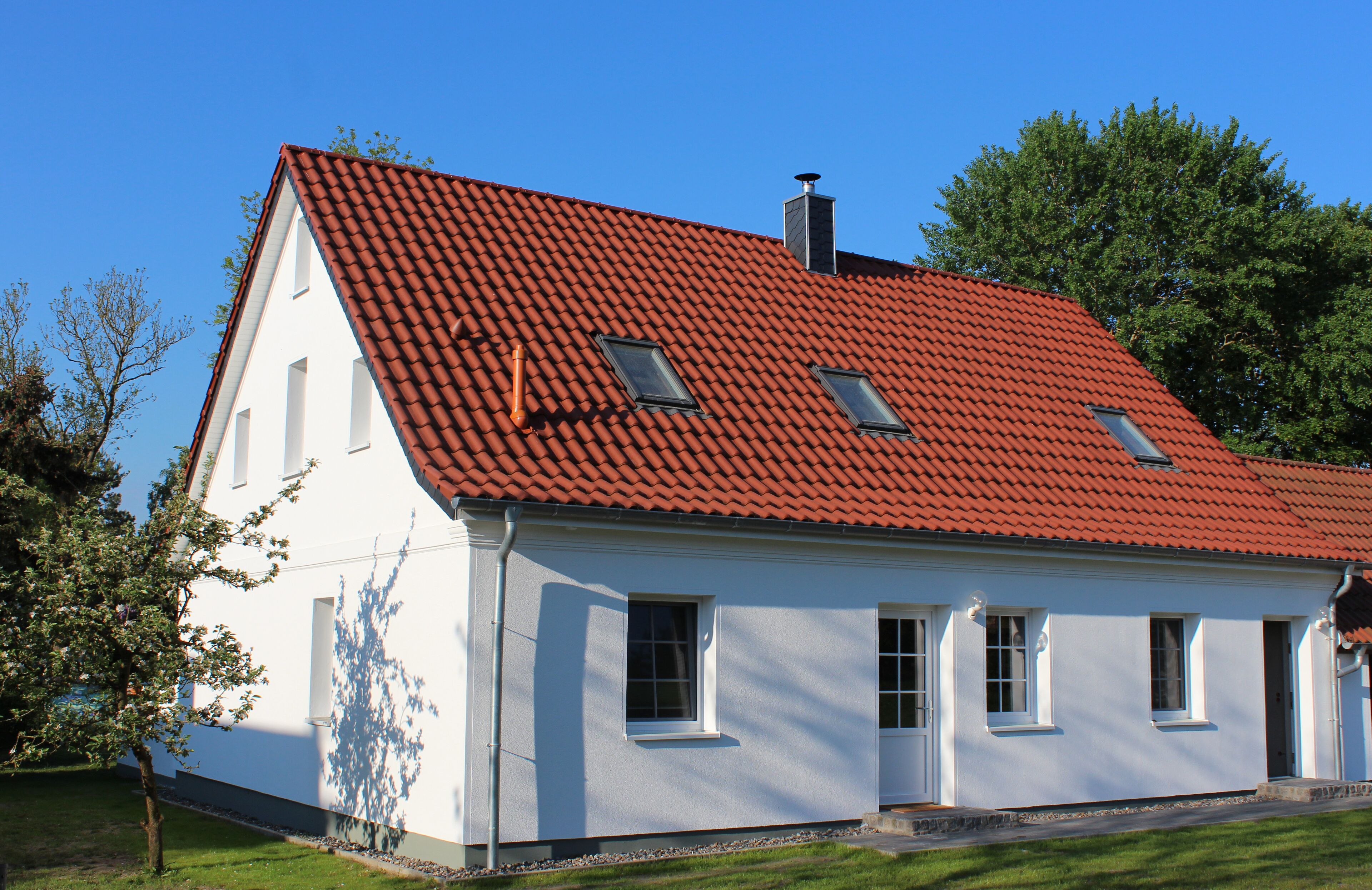 A white building with a red-tiled roof, multiple windows, and a chimney.