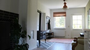 Ett rymligt rum med parkettgolv, en öppen spis, ett element, ett fönster med persienner och en hängande lampa.