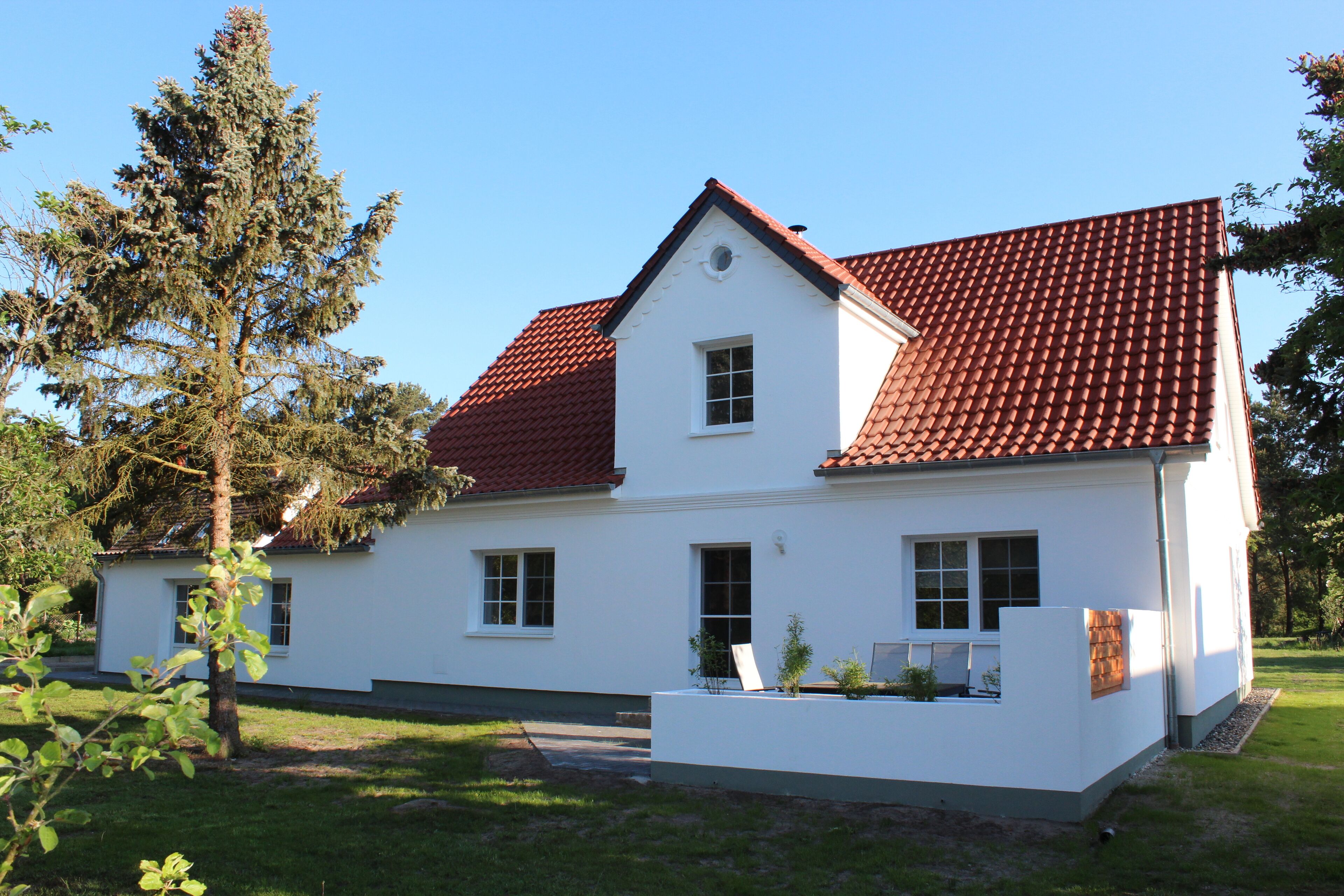 A two-story white house with a red-tiled roof, a small porch, and a well-maintained lawn.