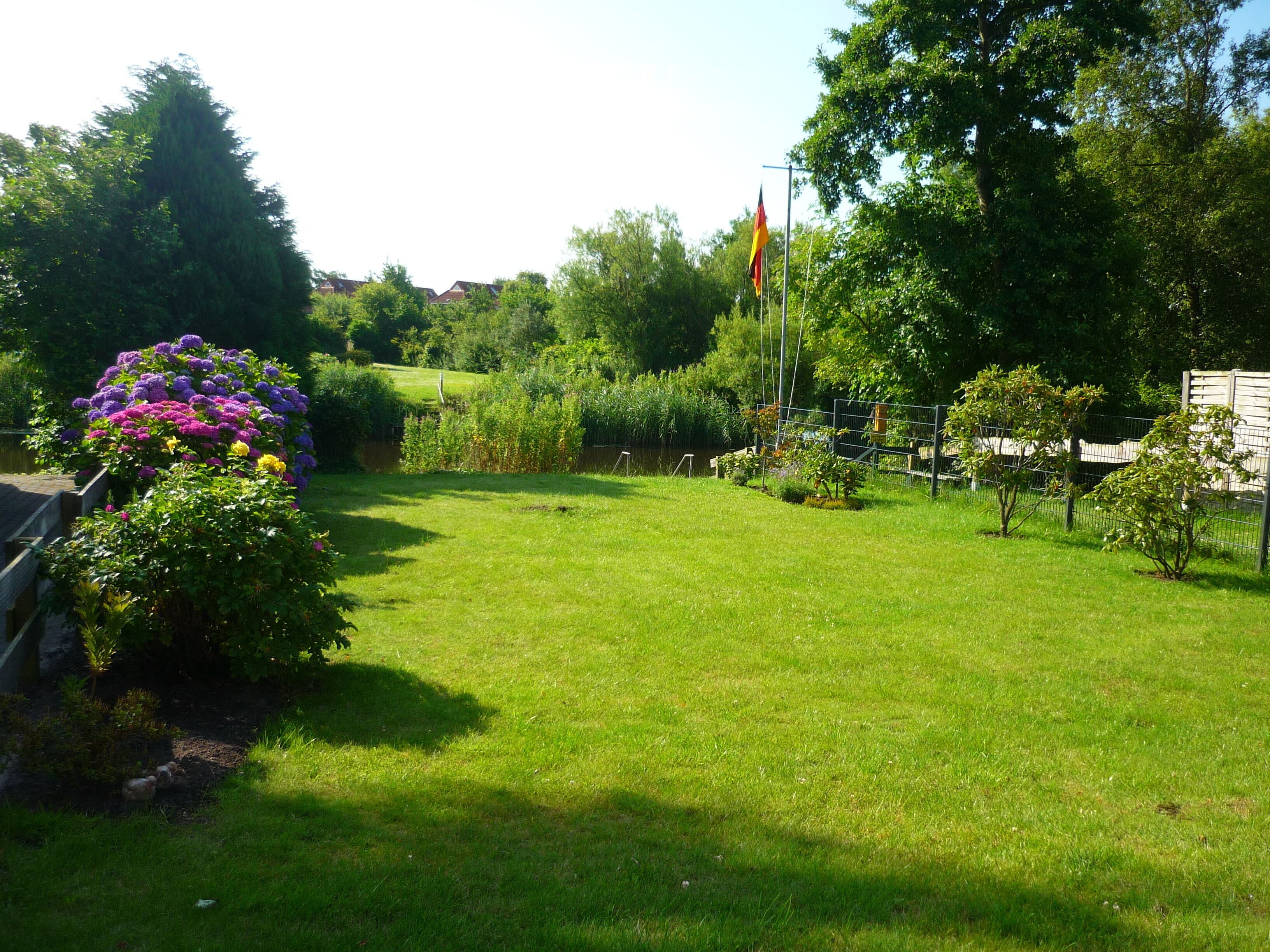 Un jardin bien entretenu, agrémenté de diverses plantes à fleurs et d’un mât pour drapeau.