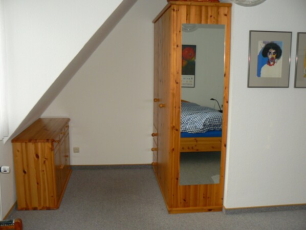 A bedroom with a wooden wardrobe, a bed with a checkered bedspread, and two framed pictures on the wall.