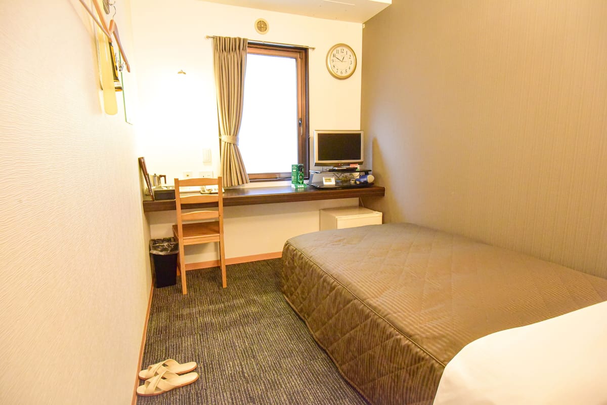 A hotel room with a bed, desk, chair, and a window with curtains.