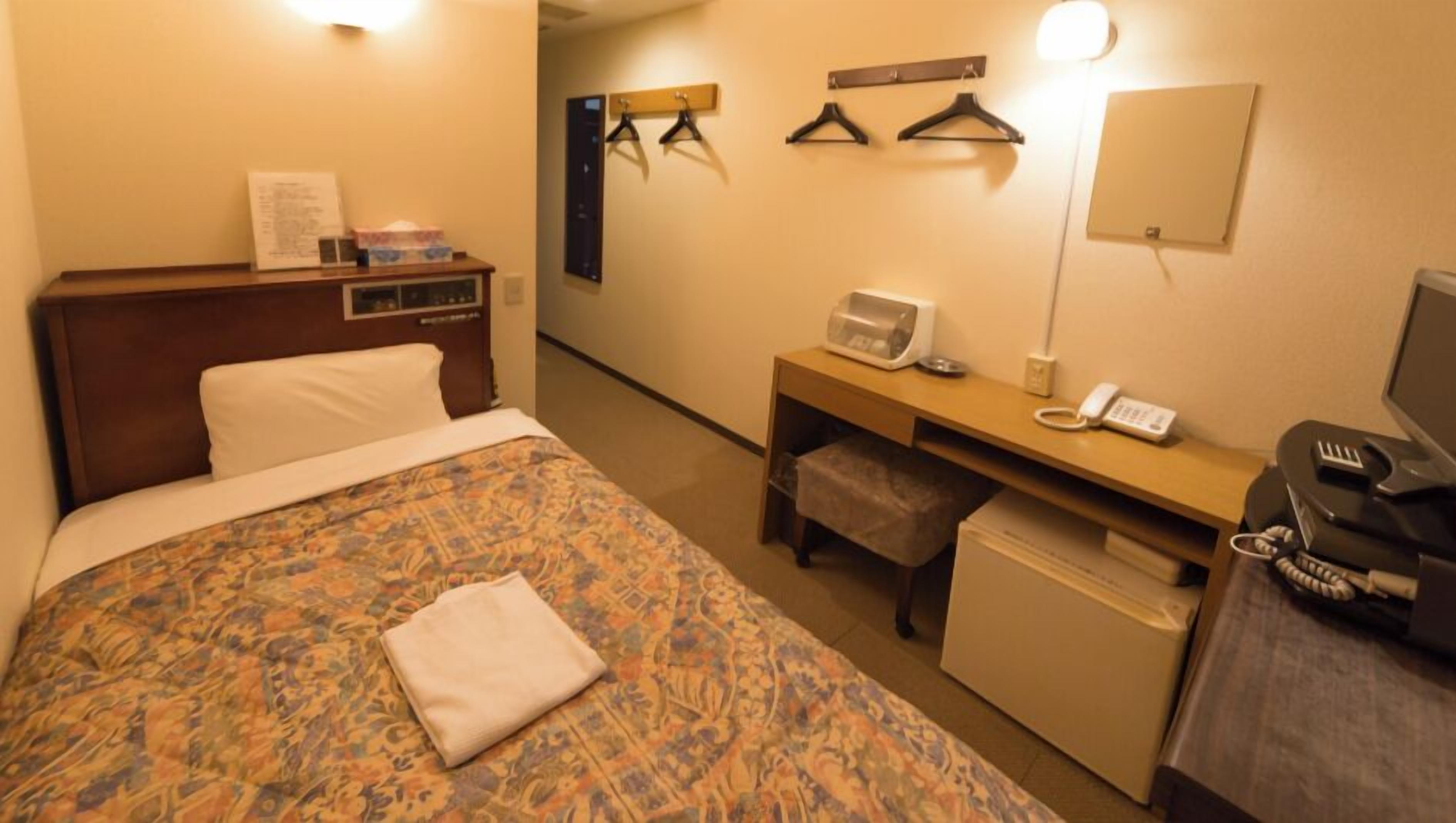 A hotel room with a bed, a desk with a telephone, a microwave, and a TV.