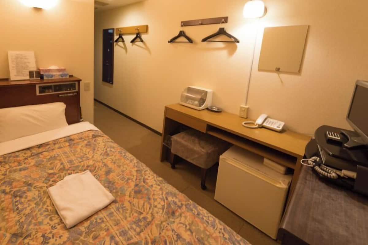A hotel room with a bed, a desk with a telephone, a microwave, and a TV.