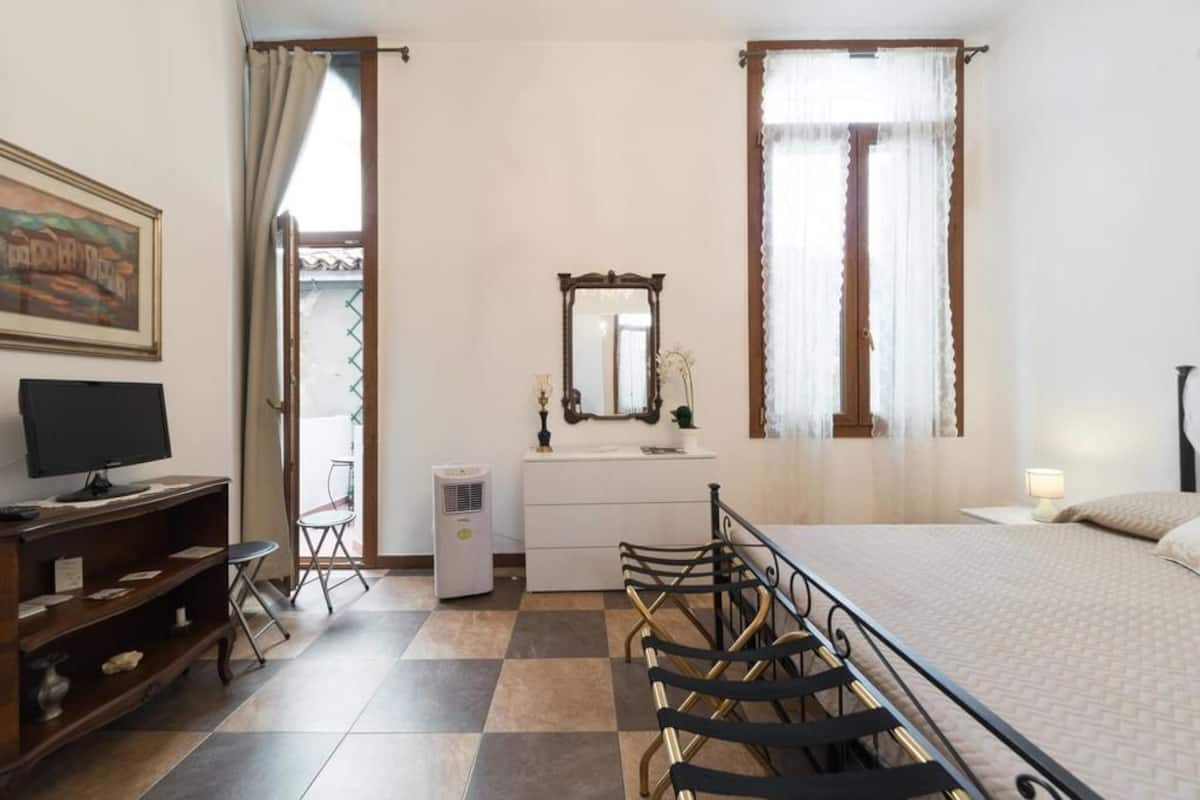 A hotel room with a bed, a desk with a computer, a chair, a dresser, a mirror, and a window with curtains.