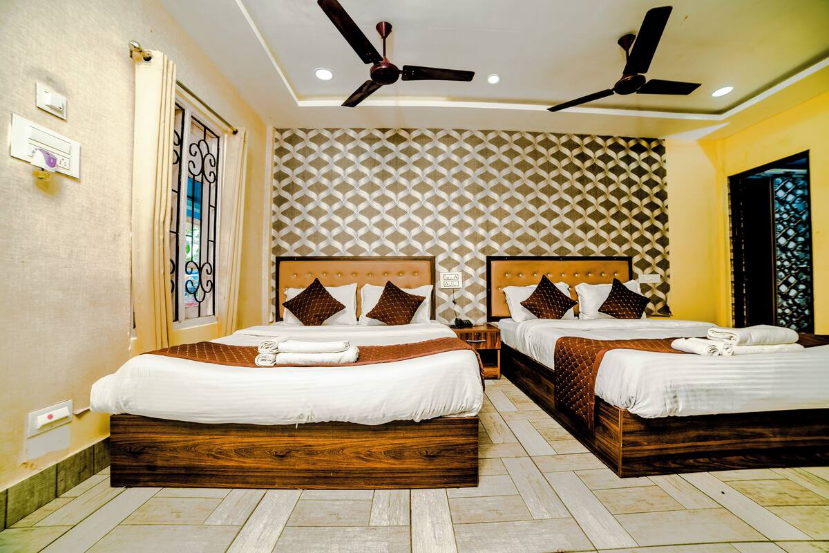 Quarto de hotel com duas camas, ventiladores no teto, parede estampada e janela com detalhes em ferro forjado.