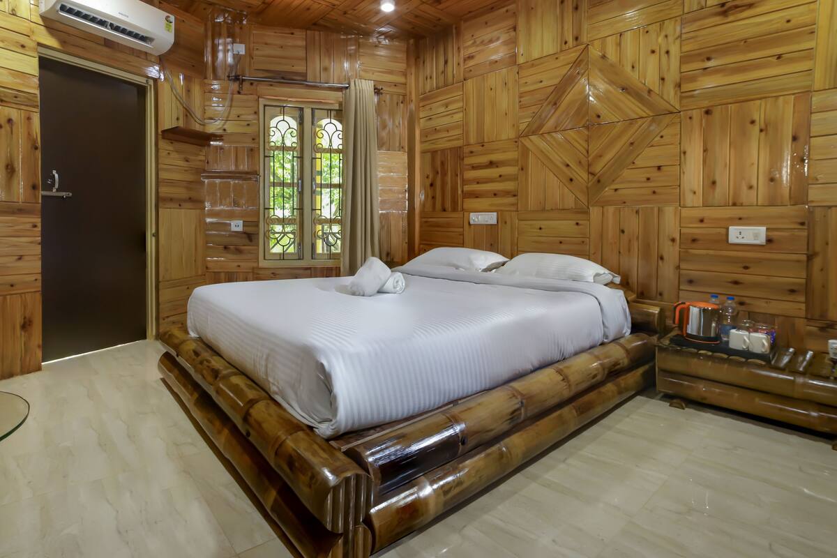 Um quarto com painéis de madeira, uma cama, uma janela com cortina e uma mesinha de cabeceira com chaleira e chávenas.
