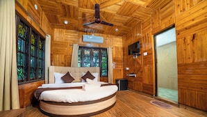 Un lit rond dans une pièce en bois, dotée d’un ventilateur de plafond, d’une télévision et d’une fenêtre ornée de motifs en fer forgé.
