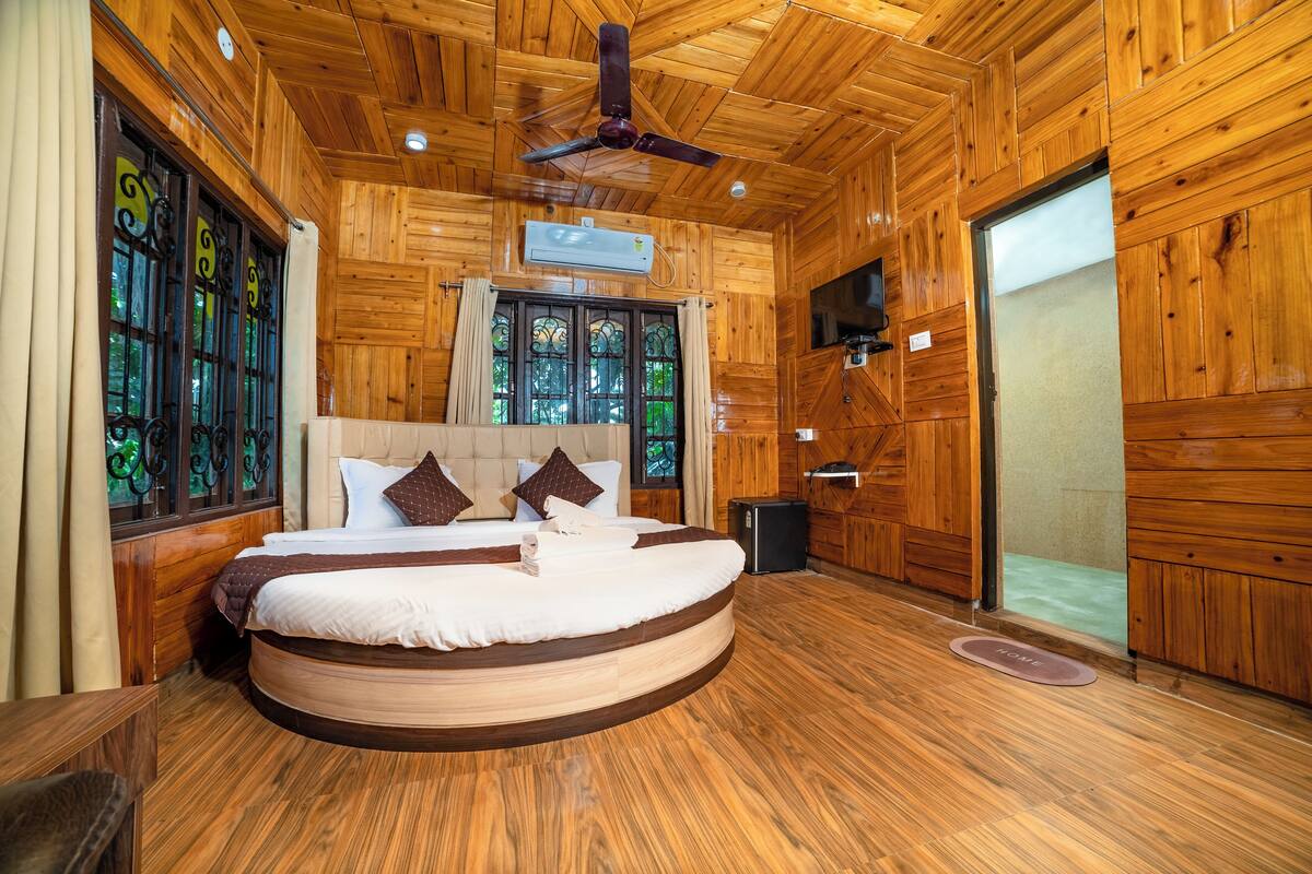 Uma cama redonda num quarto de madeira com ventoinha no teto, televisão e janela com adornos em ferro.