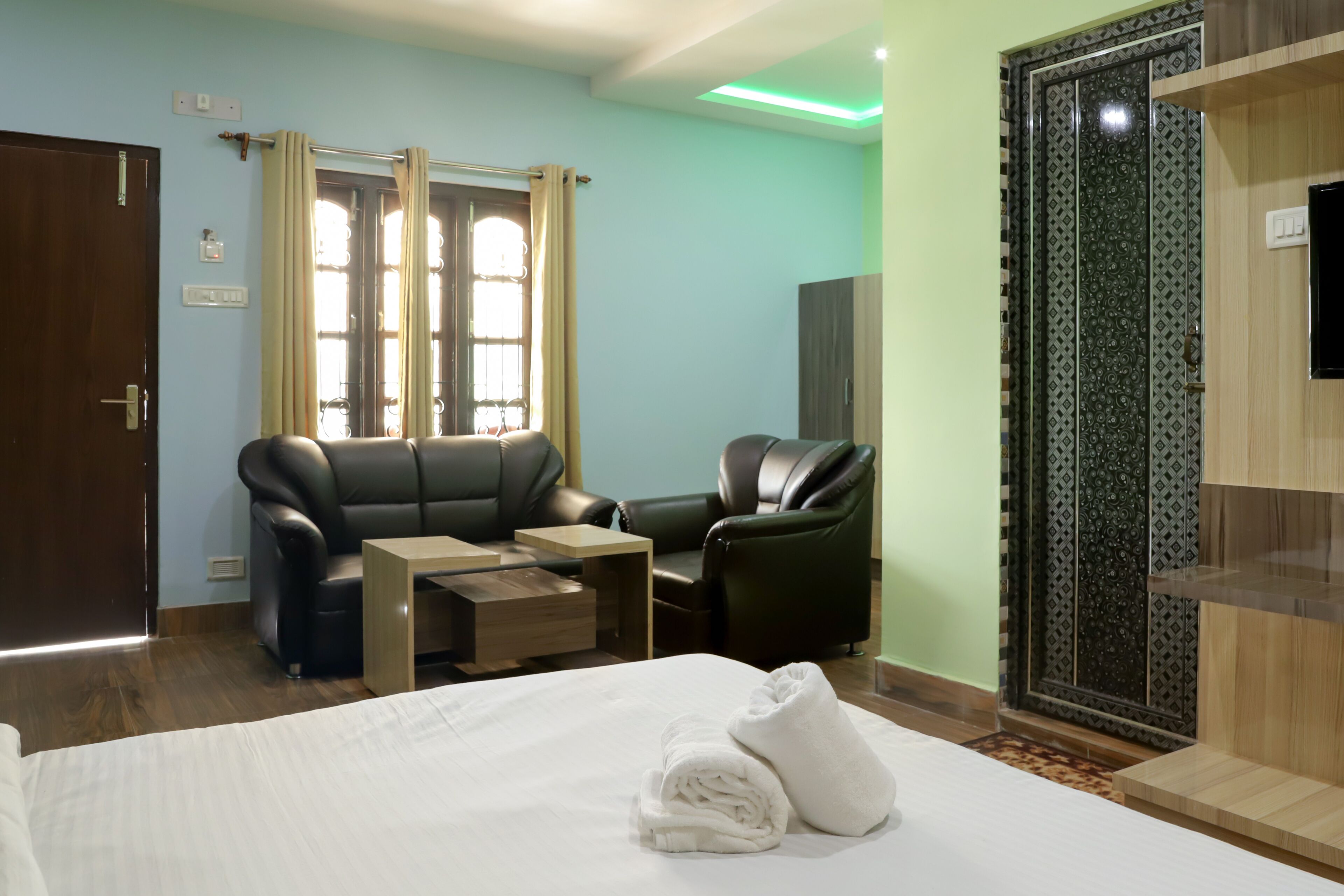 Una habitación de hotel con cama, sofá, sillón, mesita y un panel decorativo en la pared.