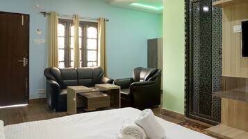 Una habitación de hotel con cama, sofá, sillón, mesita y un panel decorativo en la pared.