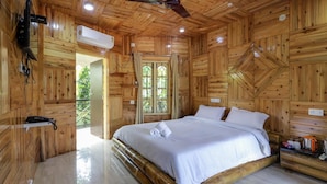Une chambre dans une cabane en bois, avec un grand lit, un ventilateur de plafond, un appareil de climatisation et une petite table avec une bouilloire.