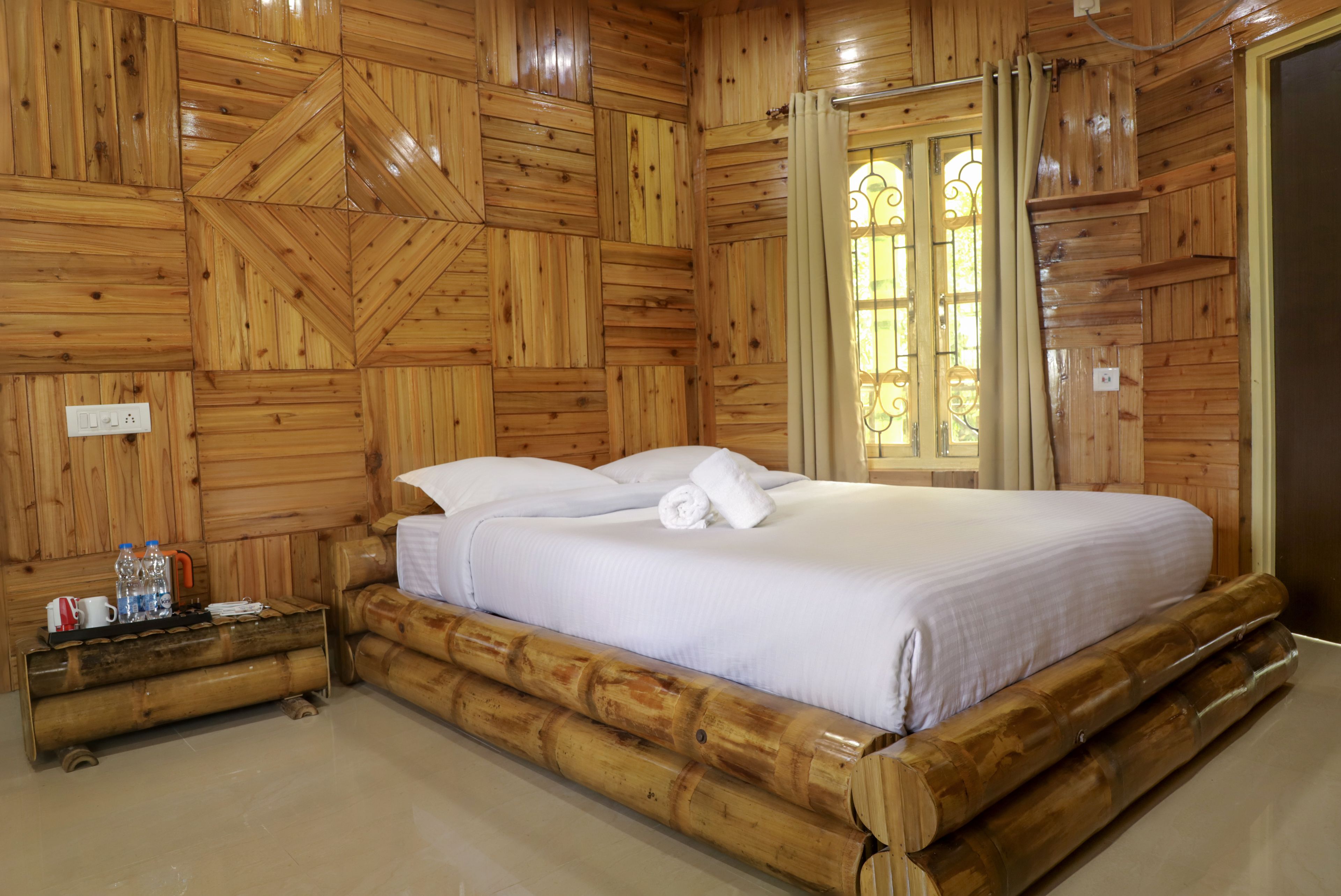 Una habitación con paneles de madera, una cama, una mesita de noche y un ventanal con cortinas.