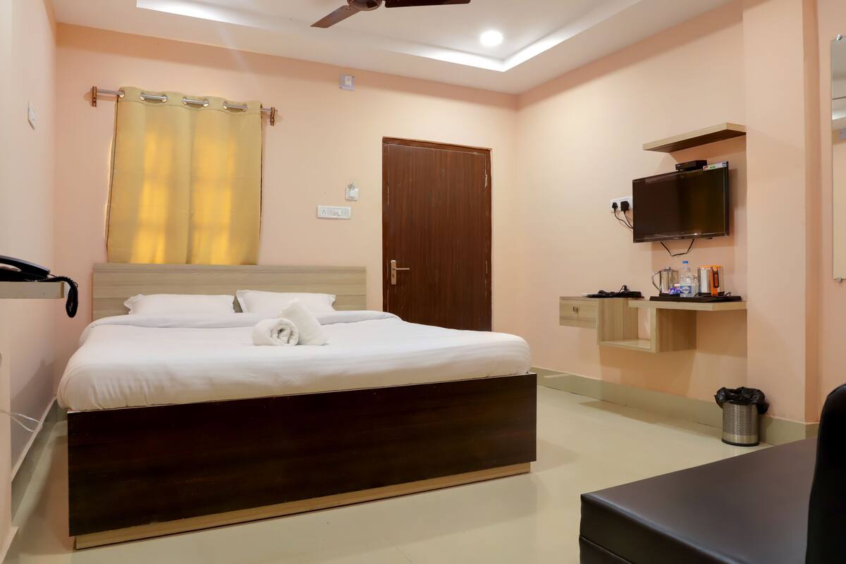 Quarto com cama, ventilador de teto, televisão e um pequeno estante com artigos de higiene pessoal.