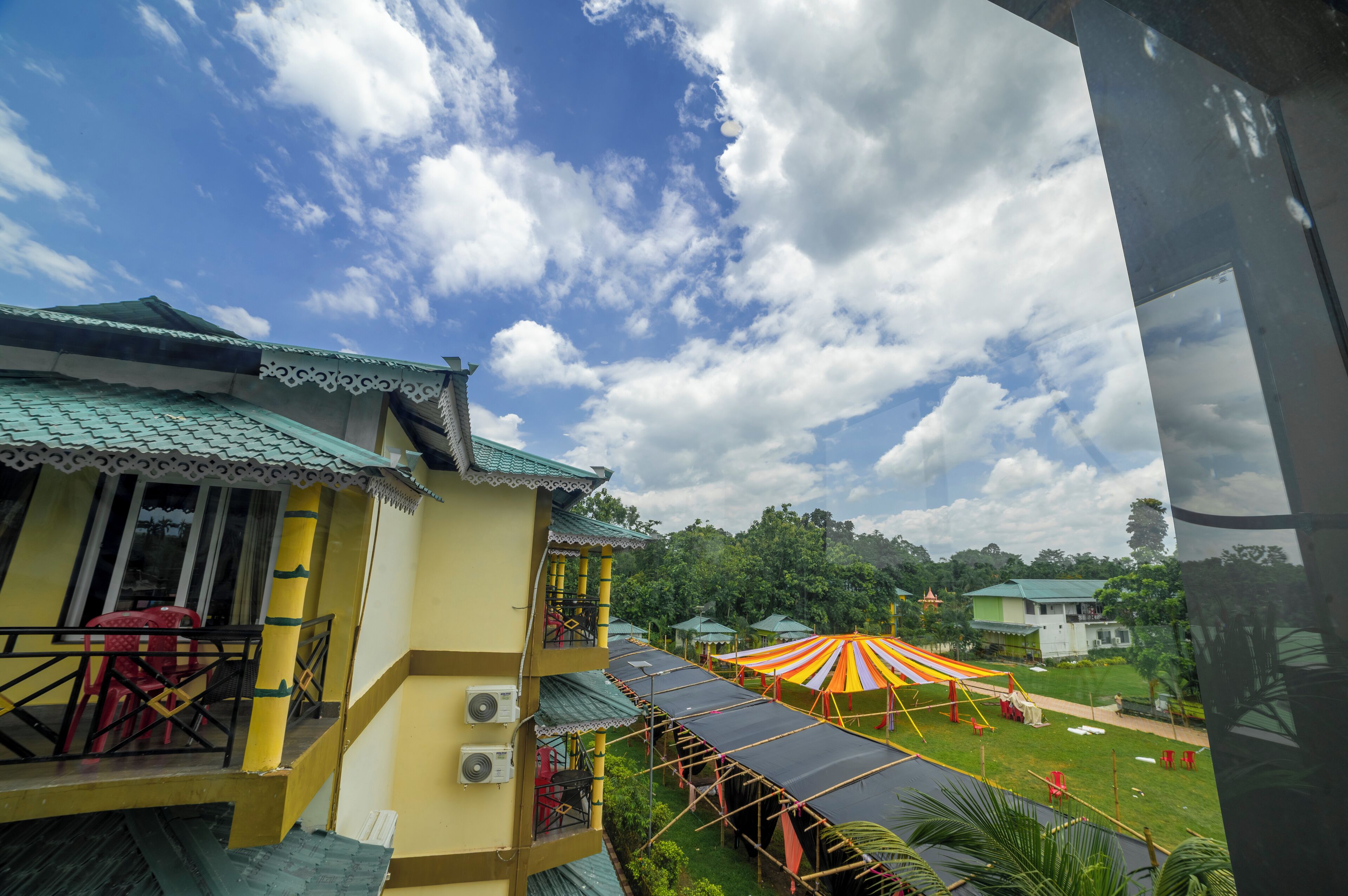 A hotel with a balcony, a covered outdoor area with a striped canopy, and a view of the surrounding greenery.