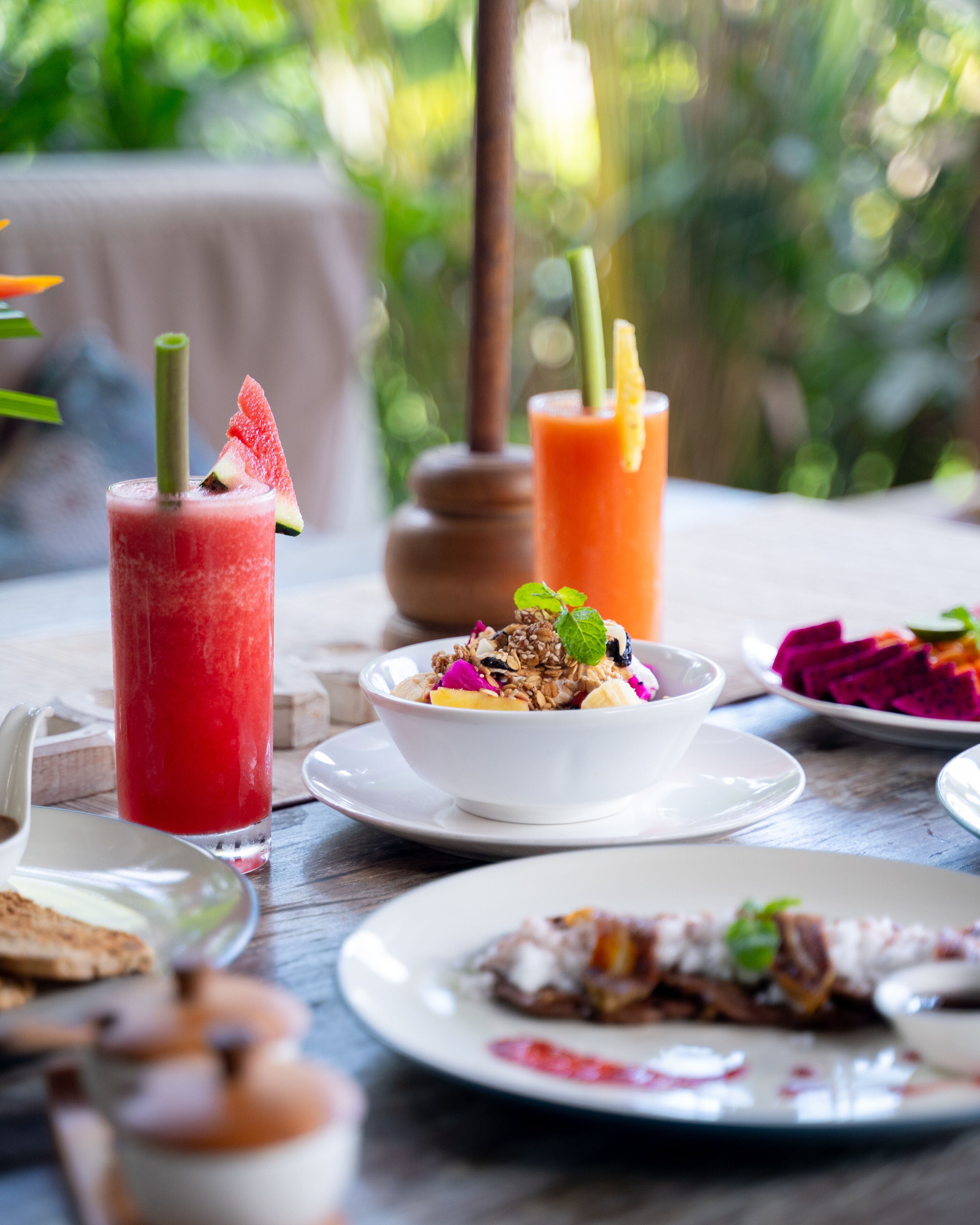 Une table sur laquelle sont disposés divers aliments et boissons, notamment une boisson à base de pastèque, un smoothie et un bol de granola aux fruits.
