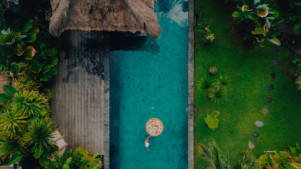 Vue aérienne d’une piscine dotée d’une structure de toit en chaume, entourée d’une végétation tropicale luxuriante.