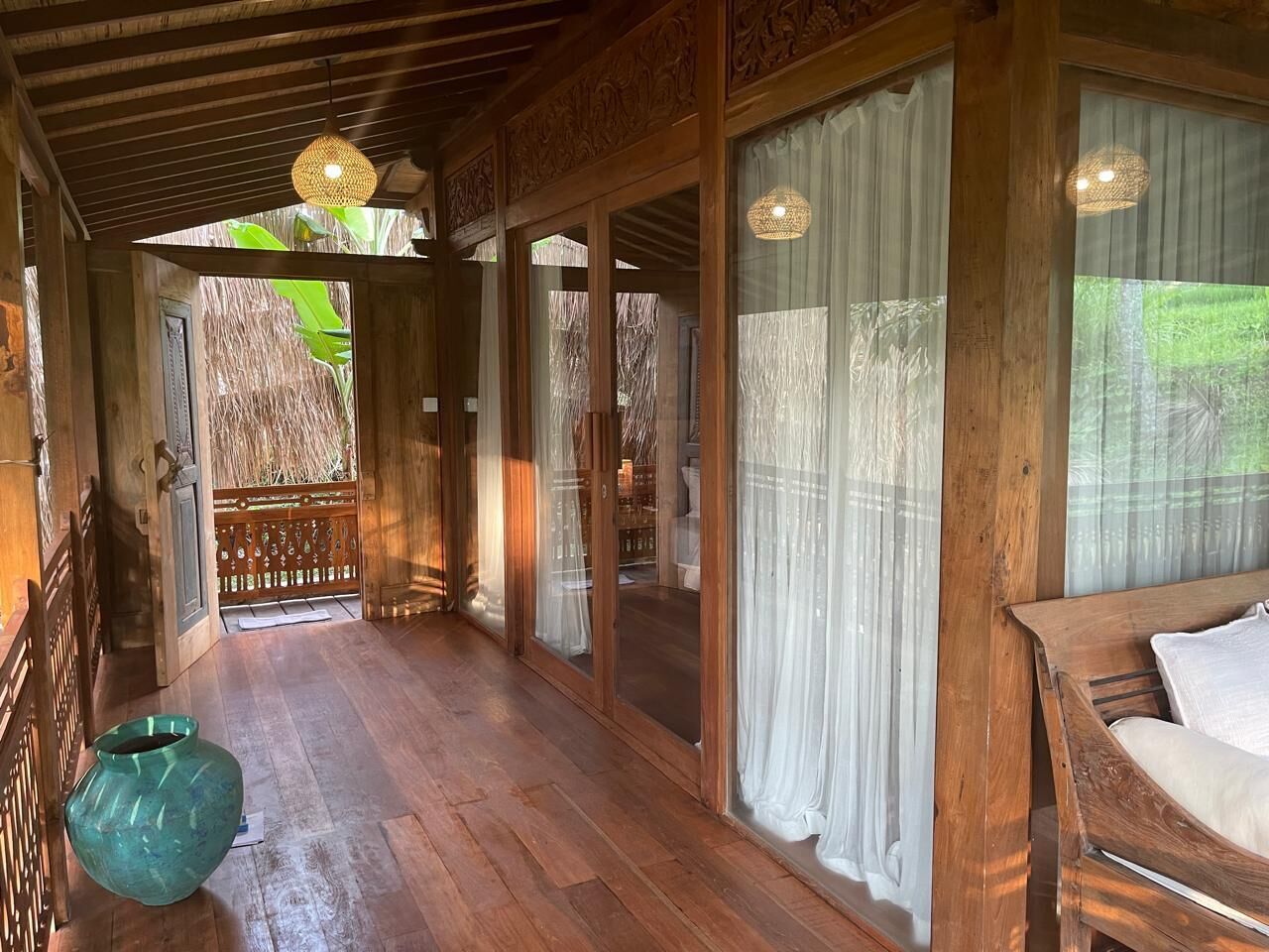 A wooden corridor with a bench, a hanging light fixture, and a view of an outdoor area through a glass door.