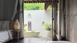 Une chambre avec un grand lit, une table de chevet, une lampe et une vue sur une salle de bain avec une baignoire et des plantes.