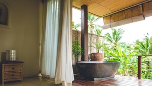 Une salle de bain avec une grande baignoire, un plancher en bois et une vue sur les palmiers.