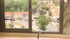 Näkymä ikkunasta, jossa on pesuallas ja hana. Ikkunasta avautuu vilkkaan kadunäkymä, jossa näkyy autoja ja rakennuksia.