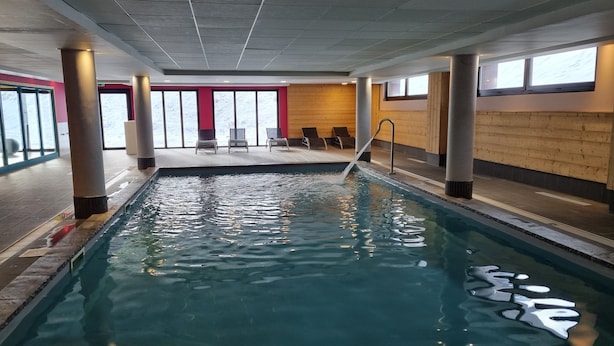 Une piscine intérieure à l’eau claire, entourée de murs recouverts de panneaux de bois et dotée de grandes fenêtres.