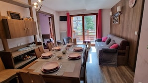 Un coin repas avec une table en bois dressée pour quatre personnes, un canapé et une vue sur l’extérieur grâce à une grande fenêtre.