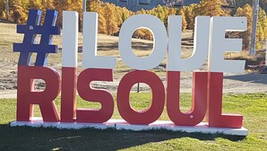 Une grande enseigne extérieure avec le texte « #J’AIME RISOU » écrit en caractères gras.