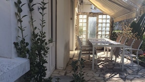 Une terrasse avec une table et des chaises, un espace couvert doté d’un toit décoré, et un mur recouvert de plantes grimpantes.