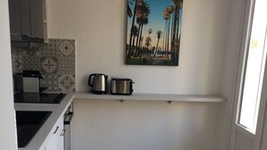 Une cuisine compacte avec un plancher en bois, un tableau représentant des palmiers et un petit comptoir sur lequel se trouvent une bouilloire et un grille-pain.
