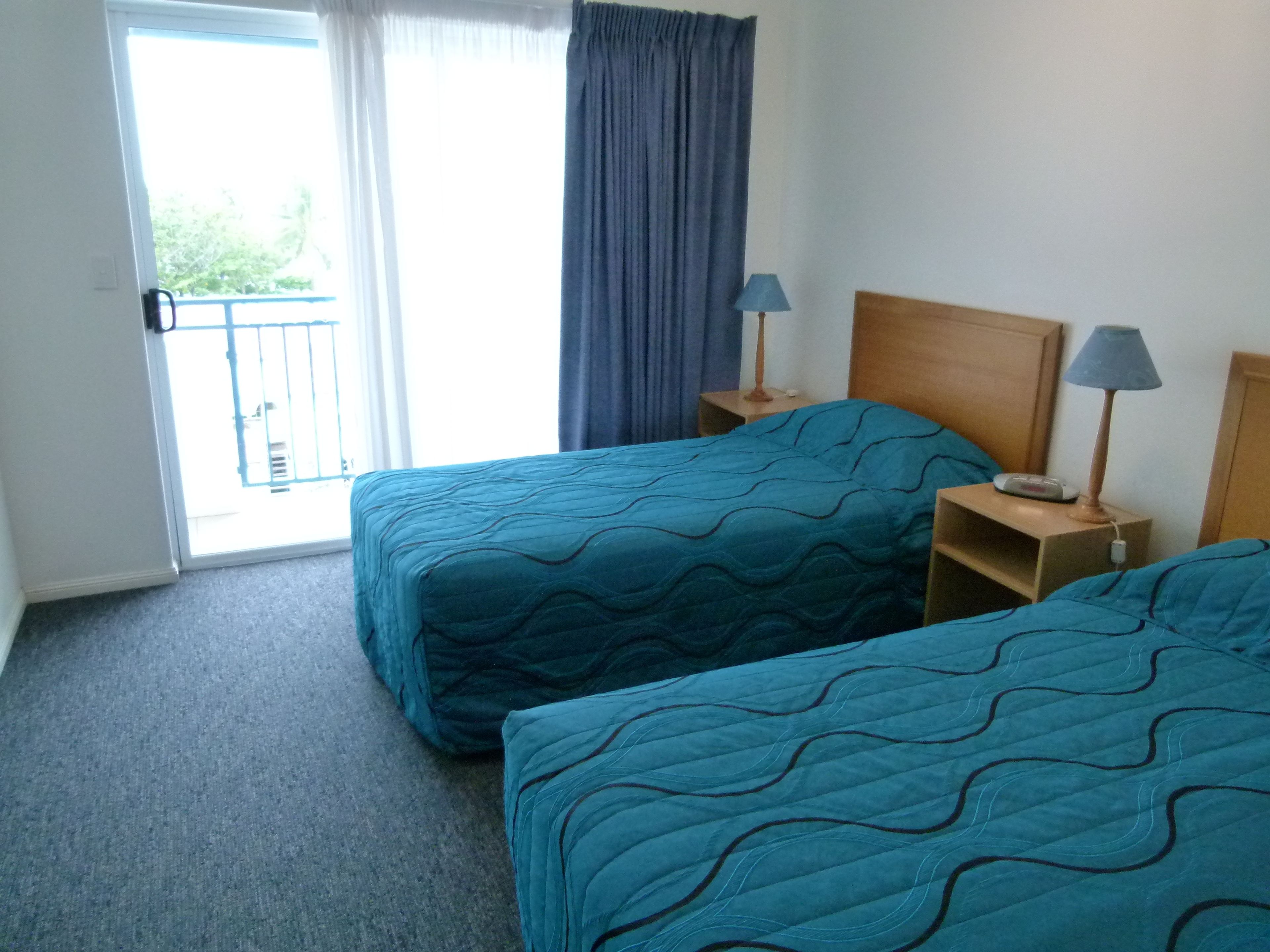 Een hotelkamer met twee bedden, een balkon en een raam met gordijnen.