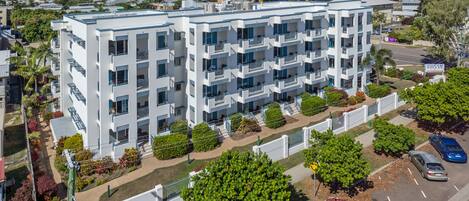 Un edificio residencial de varios pisos con balcones, un estacionamiento y vistas del entorno.
