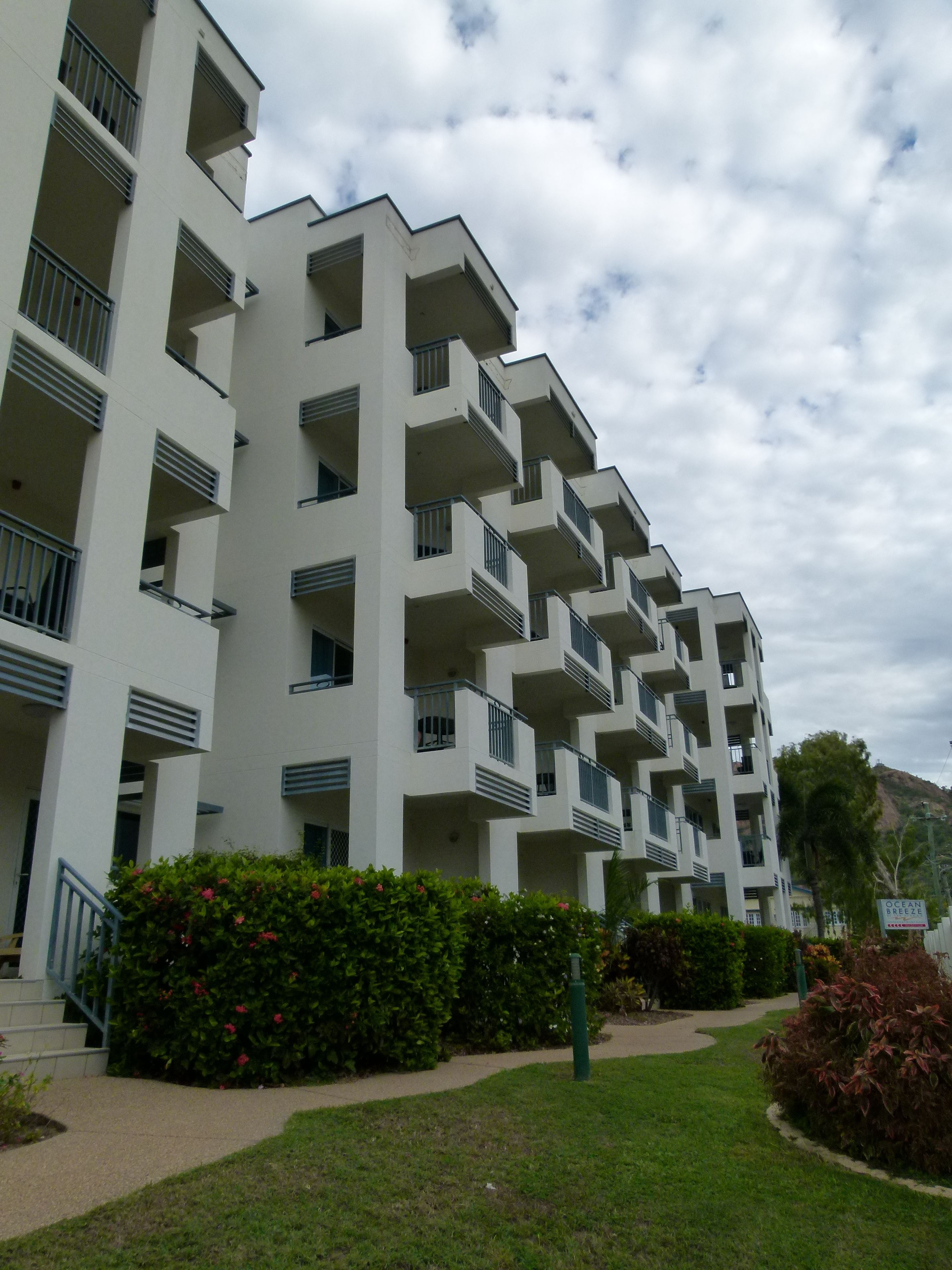 A multi-story residential building with balconies, a landscaped garden, and a sign indicating 'Ocean Breeze'.