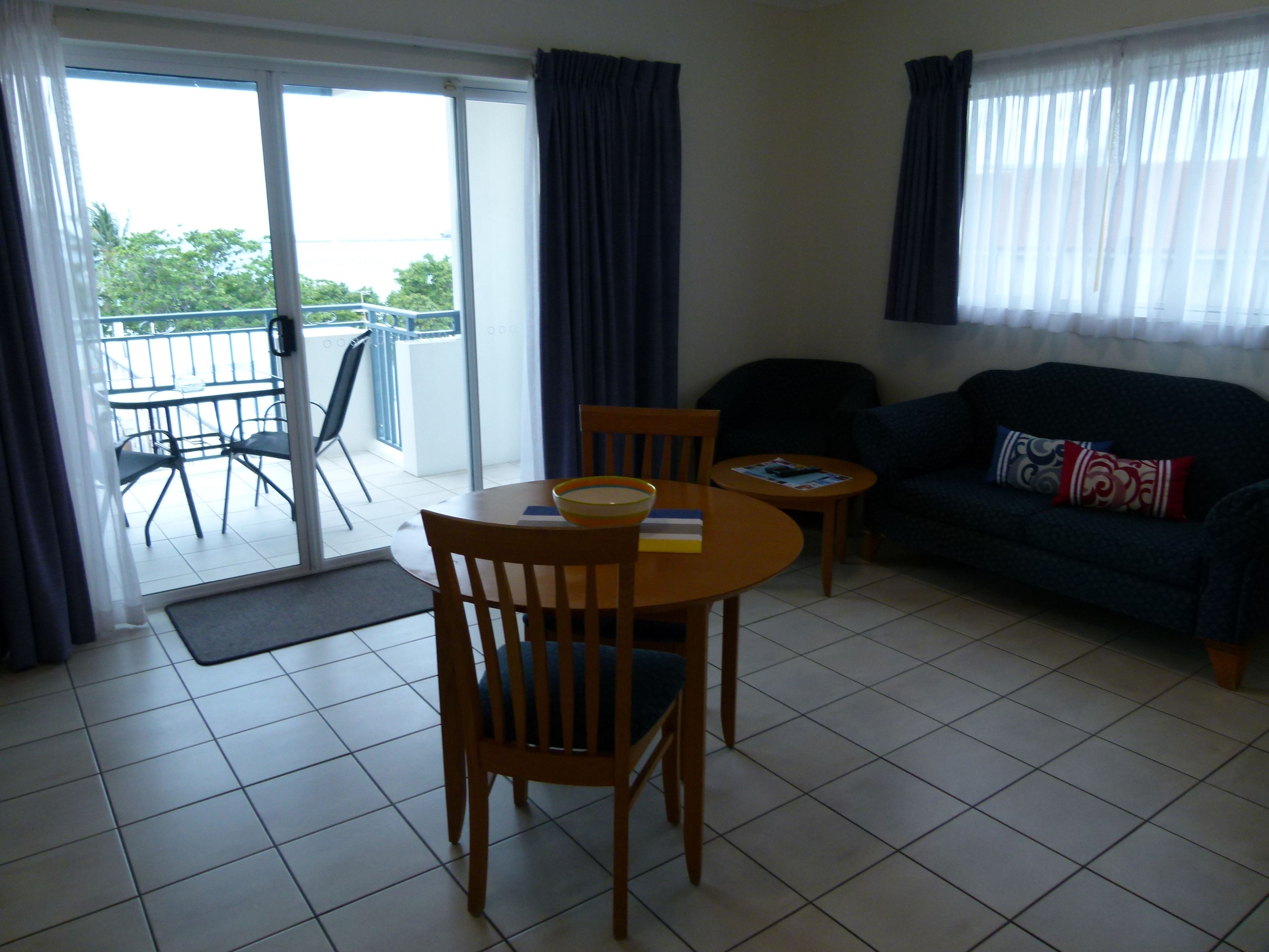 A living room with a sofa, two chairs, a small table, and a balcony with a chair and table.