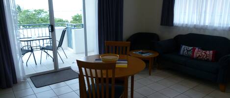 A living room with a sofa, two chairs, a small table, and a balcony with a chair and table.