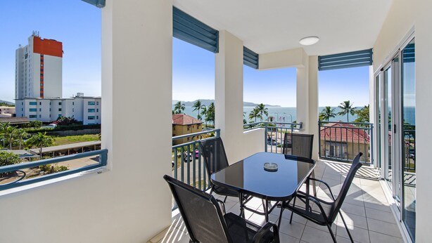 A balcony with a table and chairs, offering a view of the ocean and palm trees.