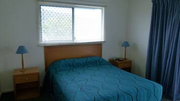 Un dormitorio con una cama individual, dos mesitas de noche, un ventanal con persianas y una cortina.