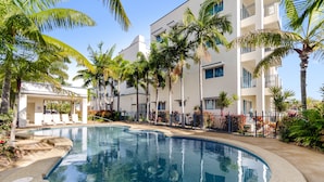 A swimming pool surrounded by palm trees and a white building with balconies.
