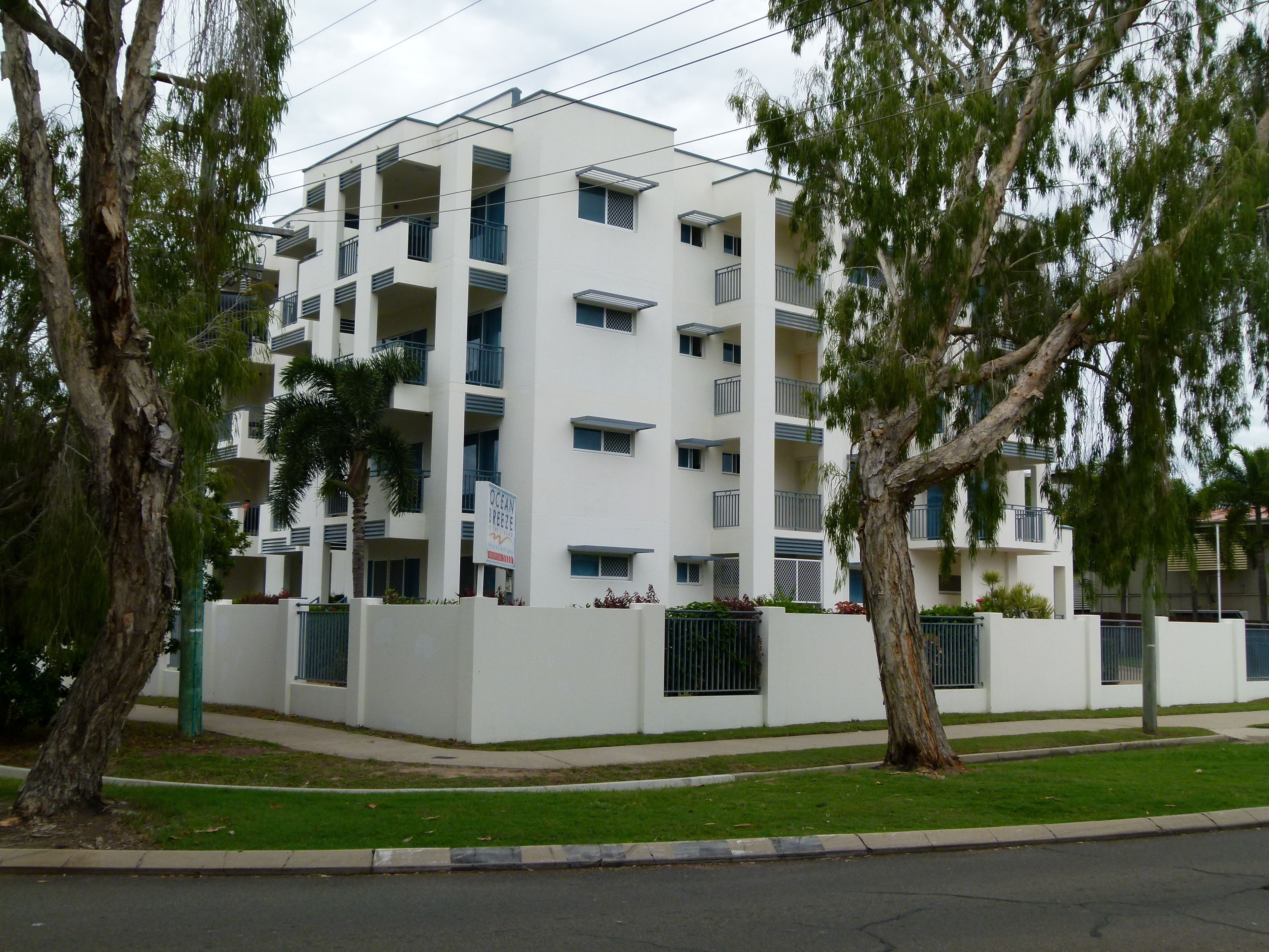 A multi-story white building with balconies, surrounded by trees and a well-maintained lawn.