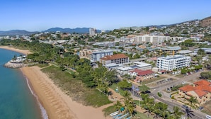 An aerial view of a coastal town with a beach, buildings, and palm trees.