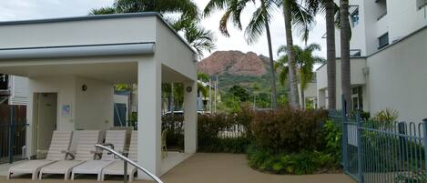 A pool area with lounge chairs, a small building, and palm trees.